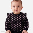 A baby girl wearing a black long-sleeve top with a pink cherry blossom pattern, photographed against a clean white background.